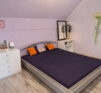 A bedroom in a family house with purple walls, a bed, a wooden decor floor, and decorations.