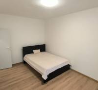 A bedroom in a studio apartment with a bed, white walls, and a floor with a wooden decor.