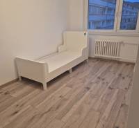 A room in a three-room apartment with a white bed and a wooden decor floor.