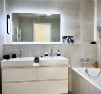 A bathroom in a 3-room apartment with two sinks, a bathtub, and a large mirror.