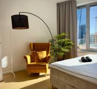 A bright bedroom in a three-room apartment with a striking chair, lamp, and plant.