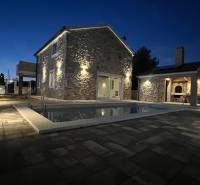 A family house in Vrsi on Vrsi Street with a stone facade and lighting by the pool.