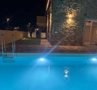 A family house in Vrsi with a pool and a stone facade illuminated by night lights.