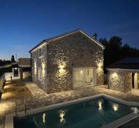 Night exterior of a family house in Vrsi with a stone facade and a pool on Vrsi street.