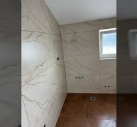 The bathroom in the family house has marble tiles and a small window.