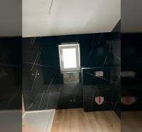 A bathroom with dark tiles and a wooden decor floor in a family house.