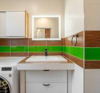 A bathroom in a 3-room apartment, with a sink, green tiles, and cabinets above the washing machine.