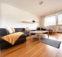 Living room of a two-room apartment with a corner sofa, a table, and a floor with a wooden decor.