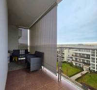 Balcony with rattan furniture, view of residential buildings and lawn in a 3-room apartment.