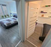 A corridor connecting the bedroom and the living room with a sofa in a 3-room apartment, with a wooden decor floor.