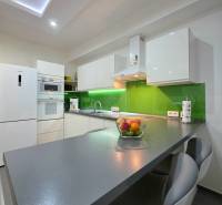 A kitchen in a 3-room apartment with white furniture and a green backsplash.