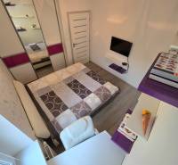 A bedroom in a 3-room apartment with a wood-decor floor, a bed, and a desk.