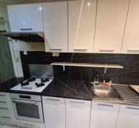 A kitchen in a 3-room apartment with an elegant white unit and black tiles.