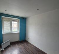 A room in a 3-room apartment with a wooden decor floor, blue wall, window with radiator.