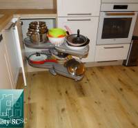 A kitchen in a 2-room apartment with a wooden decor floor and a practical corner storage system.