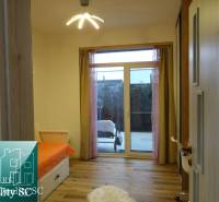 A room with a bed, a large window, and a floor with a wooden decor in a 2-room apartment.