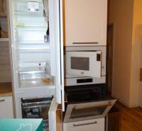 A kitchen in a 2-room apartment with an open refrigerator and oven, wooden decor flooring.