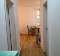 The hallway in the 2-room apartment with a wooden decor floor leads to a table and a chair.