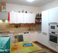 A kitchen with white cabinets and appliances, a floor with a wood decor in a 2-room apartment.