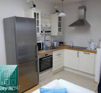 A kitchen in a studio apartment with modern equipment, stainless steel refrigerator, and white cabinets.