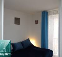 Bedroom in a studio apartment with blue curtains and decorative pillows on the bed.