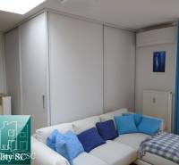A sofa with blue cushions in a studio apartment, next to a wardrobe and curtains.