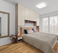 A bright bedroom with a bed, wardrobes, and a mirror in a 3-room apartment with a wood-patterned floor.