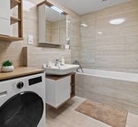 A bathroom in a 3-room apartment with a bathtub, sink, washing machine, and a floor with a wooden decor.