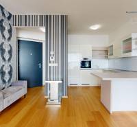 Interior of a 2-room apartment with a wooden decor floor, kitchenette, and patterned wallpaper.