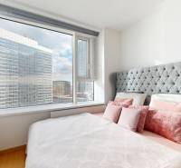 A bedroom in a two-room apartment with an upholstered bed and a view of the buildings.