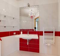 A bathroom with red and white tiles, a mirror, a sink, a washing machine, and shelves in a 2-room apartment.