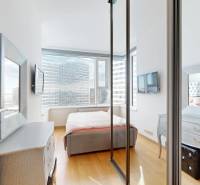 A bedroom in a two-room apartment with a wood-patterned floor and a view of the city.