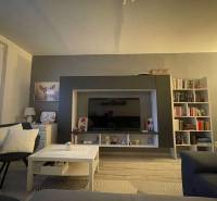 Living room with a sofa, television, bookshelf, and wooden decor flooring in a two-room apartment.