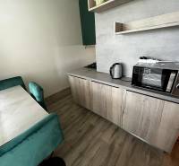 A kitchen in a 2-room apartment with a wooden decor floor, table, chairs, and appliances.