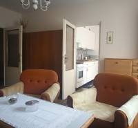 Living room of a two-room apartment with orange sofas, a display cabinet, and a view into the kitchen.