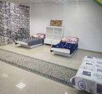 A room in a family house with three beds, a shelf, and light tiles.