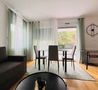 Living room of a holiday apartment with a sofa, dining table, and wood-patterned flooring.