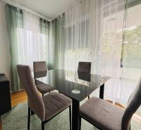Dining area in a holiday apartment with wood-patterned flooring and sheer curtains.