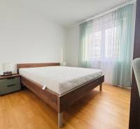 Recreational apartment with a bed, nightstand, light curtains, and a floor with a wooden decor.
