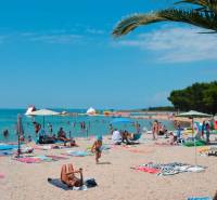 Sandy beach in Povljana near the holiday apartment with many visitors under umbrellas.