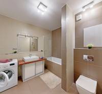 Bathroom with light tiles, a bathtub, and a washing machine in a 3-room apartment.