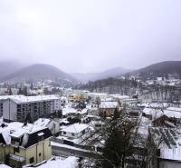 Snow-covered town of Trenčianske Teplice from Gogoľova Street with a view of the surrounding hills.