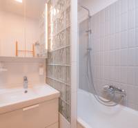 Bathroom in a 3-room apartment with a sink, mirror, and a bathtub with a glass wall.
