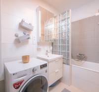 A bathroom in a 3-room apartment with a shower, a washing machine, and light tiles.
