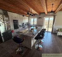 A kitchen in a family house with an island, a wooden decor floor, and a view outside.