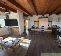 Living space with a wooden ceiling, wood-patterned floor, and a tiled stove in a family house.