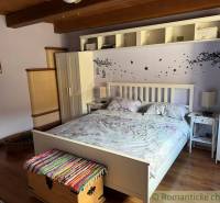 A bedroom in a family house with a bed, white furniture, and a wooden decor floor.