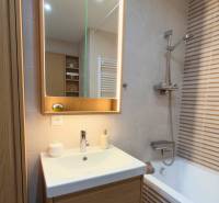 Bathroom with a lighted mirror and a bathtub in a 2-room apartment, light tiles.