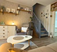 Living room with wood-patterned flooring, stairs, and light-colored furniture in a two-room apartment.