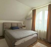 Bedroom in a two-room apartment with a double bed, curtains, and an armchair, floor with wooden decor.